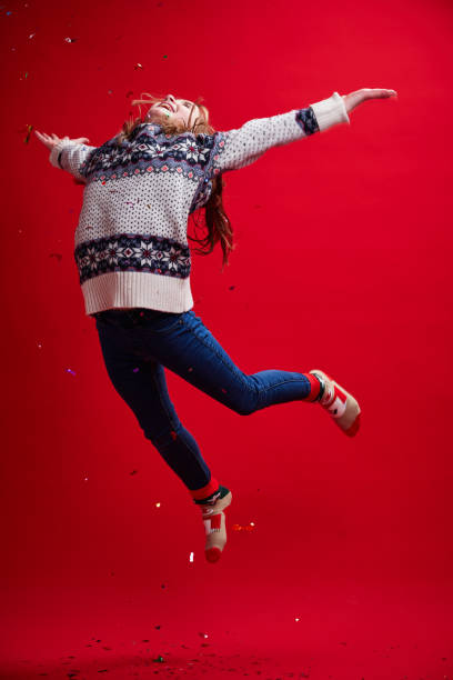 Girl in sweater and jeans jumps on red background. stock photo