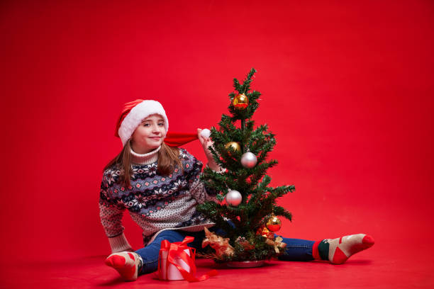 Happy girl sits on red background with Christmas tree and gift stock photo