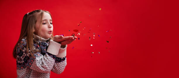 Girl on red background blows confetti off her hands stock photo