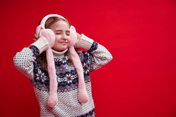 Cute girl in sweater holds with hands fluffy headphones stock photo