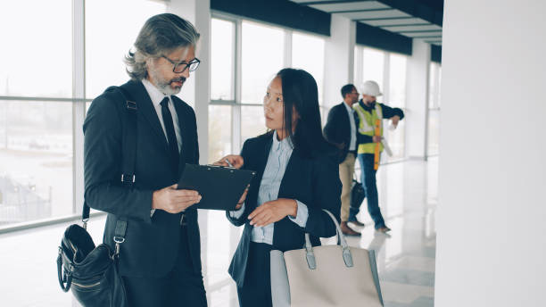 istock Multi-ethnic business partners man and woman talking in modern building while workers in uniform busy in background 1783632420