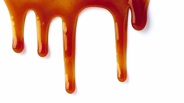 Dripping caramel drops of sweet caramel sauce. Melted caramel sauce. Pouring over white surface.
