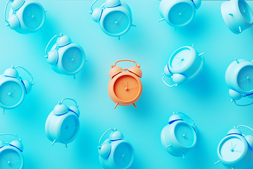 Orange alarm clock surrounded by blue alarm clocks on blue background. Horizontal composition.