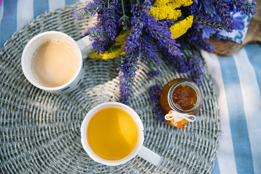 summer bouquet and a cup of tea and coffee with milk and jar of jam on a picnic blanket shot from above