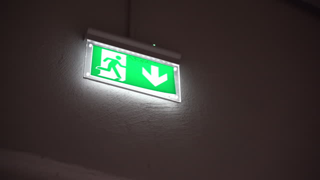 Illuminated emergency exit sign on the wall, down arrow and running person pointing the right direction to escape in case of danger, emergency exit symbol, direction for evacuation