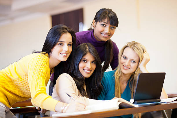 Photo of a gorgeous blond teenage student girl sitting in the library with two friends and doing homework.