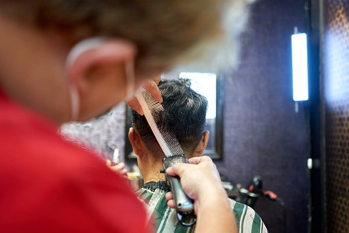 Barber cutting the hair on the nape of a client using a comb and electric razor