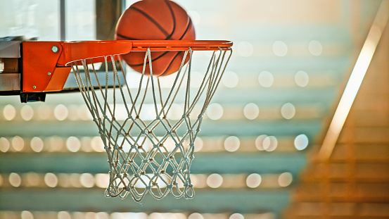 Close-up of basketball falling into basketball hoop in stadium.