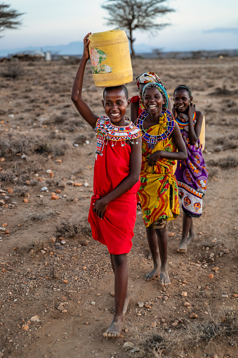 African young girls from Samburu tribe carrying water to their village, Kenya, Africa. African women and also children often walk long distances through the savanna to bring back containers of water. Some tourist camps cooperating with nearby villages and allow local people to use their water. Samburu tribe is north-central Kenya, and they are related to  the Maasai.