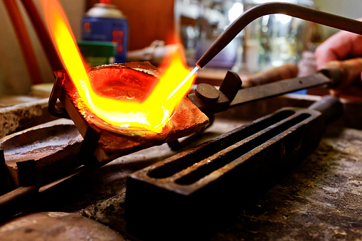 Heated to red-hot melting point by a blowtorch, pure silver in a jeweler's crucible among molds and tools of the trade.