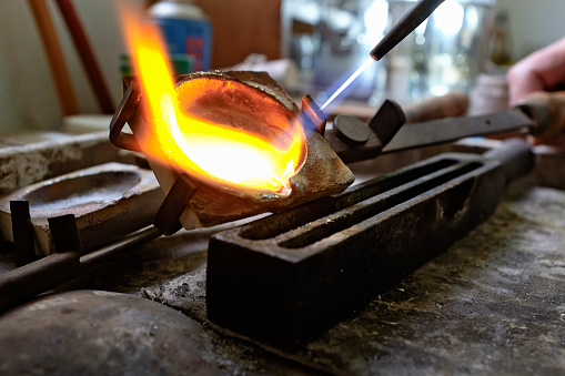 Heated to red-hot melting point by a blowtorch, pure silver in a jeweler's crucible among molds and tools of the trade.