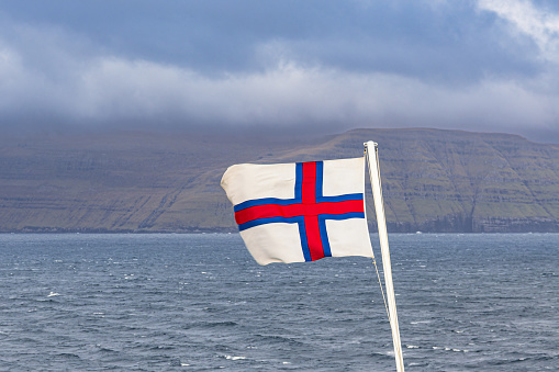 Flag in front of the rocks of the Faroe Islands with clouds.