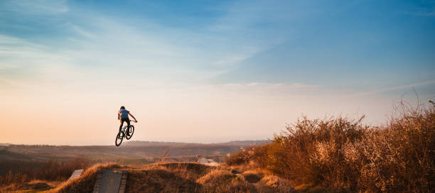 Skillful mountain bike cyclist practiocing in nature and practicing backflip against the sky.