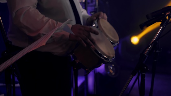 Bongo drum percussionist in white classic shirt and bass player perform on stage