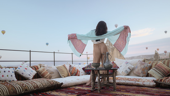 Portrait of young female tourist watching hot air ballons from balcony in Cappadocia during her travel.