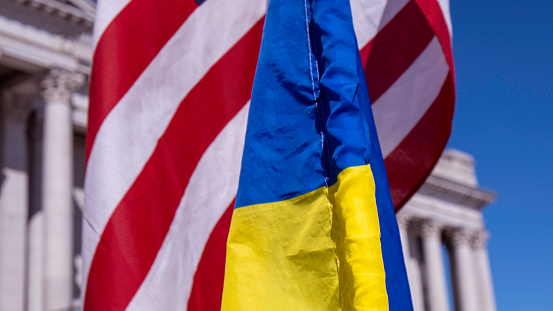 Close up of US, Ukraine flags overlapping each other with capitol building in background on a sunny day