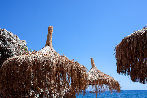Straw umbrella or thatched hut with beautiful sky view on the tropical beach. Beach straw umbrellas against clear blue sky.