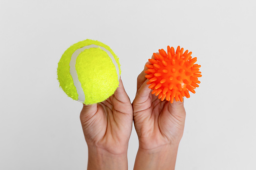 Spiky orange massage needle ball and yellow tennis ball in child hands