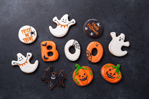 Halloween gingerbread cookies: text BOO, bats, pumpkins and ghosts on dark stone background. Halloween concept