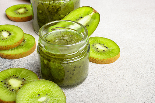 Homemade kiwi jam in a jar and kiwi slyces on concrete background with copy space