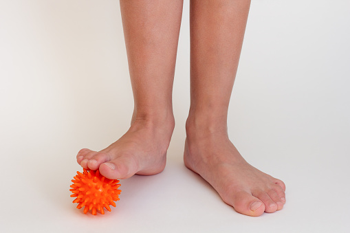 Cropped child legs doing exercises with spiky needle ball