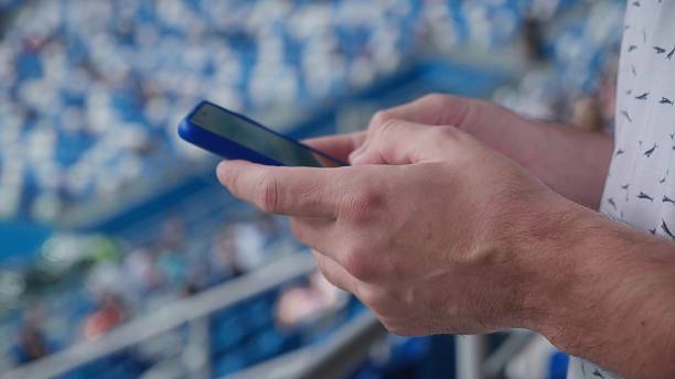 istock A young man writing a message on his phone during a match at the stadium. 1783689735