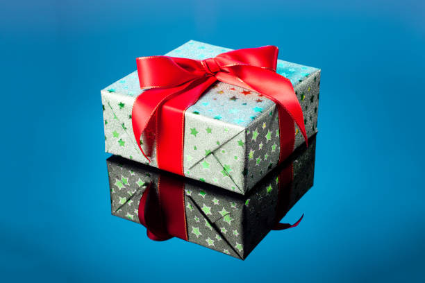 istock Single green gift box with red ribbon bow on blue reflective surface. Gift box wrapped in green shine paper with red ribbon. 1783690975