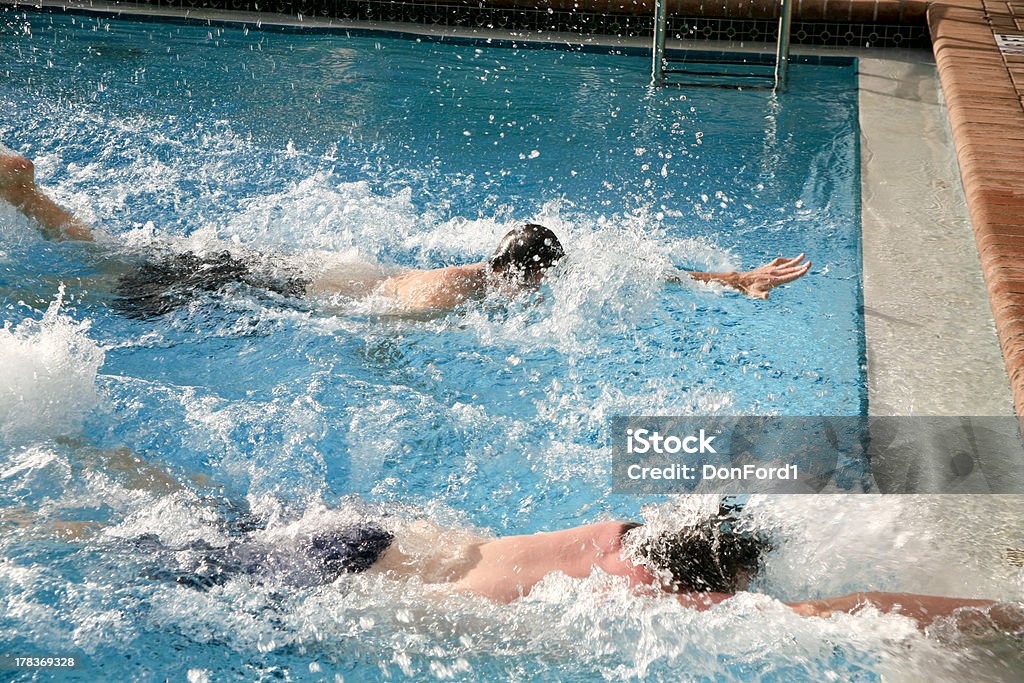 Two male swimmers racing to touch the wall in a pool Two young men reaching for the finish, the second place guy is just inches away. The action is blurred to show the excitement of the moment. Blurred Motion Stock Photo