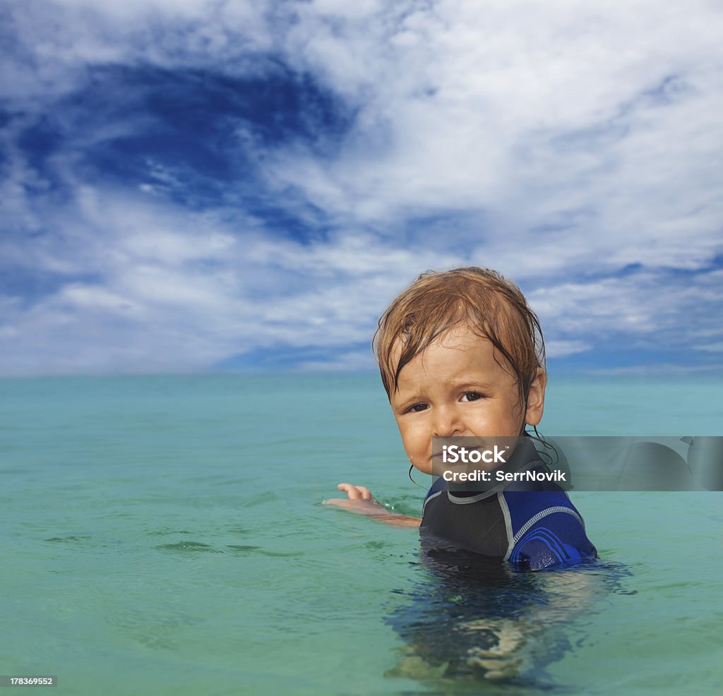 cute kid in wetsuit Toddler standing in the water with wandering expression on the face 12-17 Months Stock Photo