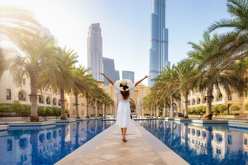 A happy tourist woman in a white summer dress walks through the streets of Dubai, UAE, during her holiday time