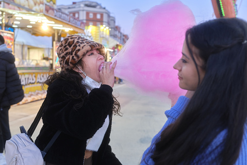 Two friends sharing a big pink cotton candy in a evening fair