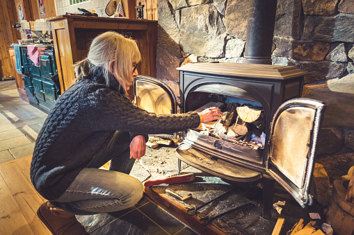 Woman lighting a wood burning stove with a match. The glass doors might just be about needing a clean.