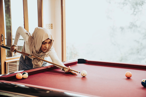An Asian  muslim girl in hijab (Veil) playing billiard indoor at home