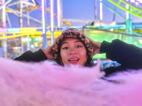 Surprised woman in front of a cotton candy ball at an evening fair