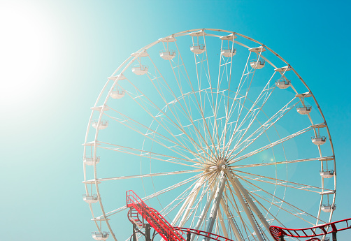 Amusement park on sunny day with close up Ferris wheel and roller coaster. Summer family fun on vacation