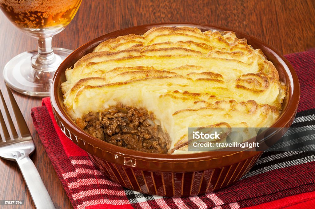 Cottage pie in a brown dish next to a fork and glass of wine Cottage or Shepherd's Pie with a glass of beer. Savory Pie Stock Photo