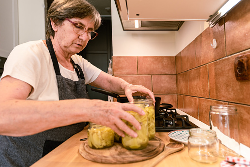 Senior Woman in Domestic Kitchen Preserving Fresh Organic Bell Peppers in Glass Jars for Winter