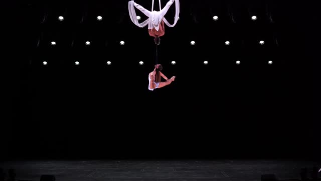 Aerial silk duo with white costume on black stage background performing at high altitude