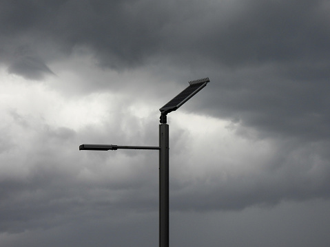 Solar panels supply energy to this streetlight located in the park above Bondi Beach, Sydney.  Spikes have been placed at the top of the panels to deter birds from perching.  In the distance are storm clouds from a severe storm passing through Sydney.  This image was taken on a windy, rainy and overcast afternoon on 9 November 2023.
