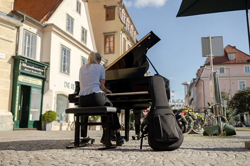 A girl plays a black piano on the street of an old European city