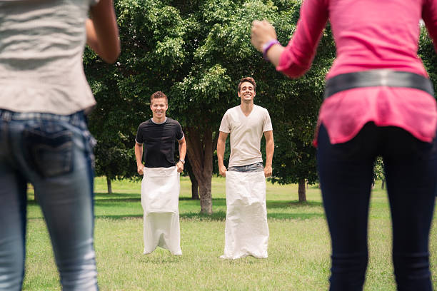 men playing sack race with girlfriends cheering stock photo