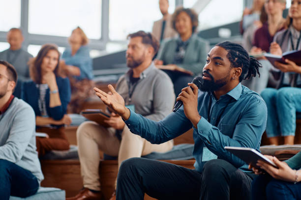 istock Black business seminar attendee asking a question while sitting in audience at convention center. 1783739895