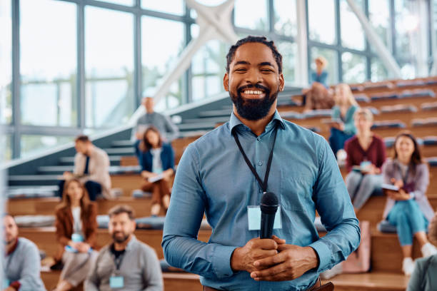 Happy black public speaker during business conference in convention center looking at camera. Happy African American presenter an education event in conference hall and looking at camera. black man giving speech stock pictures, royalty-free photos & images