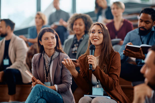istock Young happy businesswoman talking on microphone while attending education event in conference hall. 1783743147