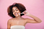 Portrait of a young well-groomed dark-skinned woman with lush hair, doing facial massage with the help of a roller with closed eyes, care and skin care