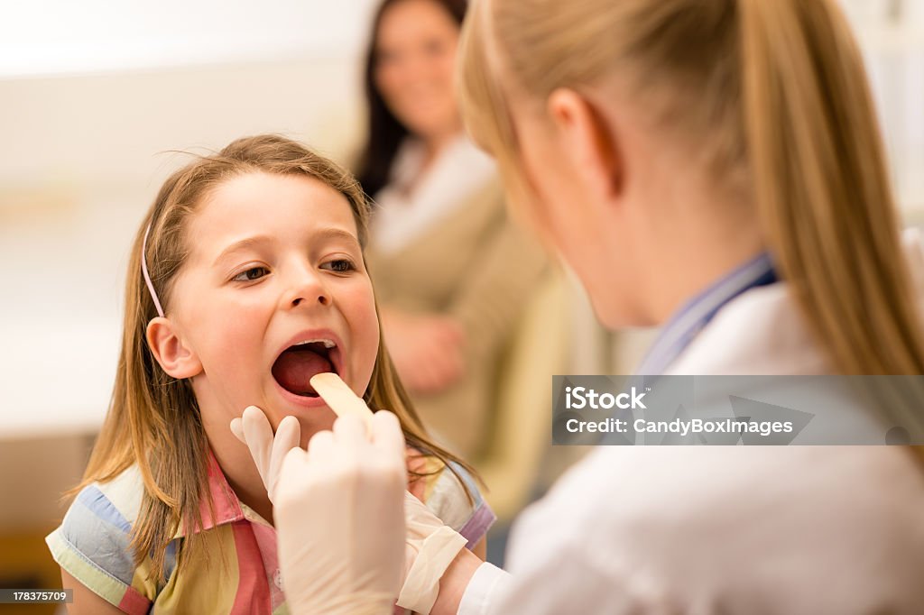 Pediatrician examining a little girl's throat Little girl having throat examination with tongue depressor Girls Stock Photo