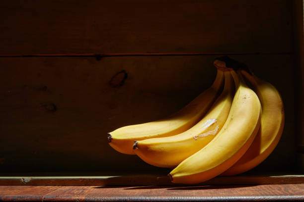 Image of bunch of ripe yellow bananas on wooden background, bright sunlight, harvest in wooden box. stock photo