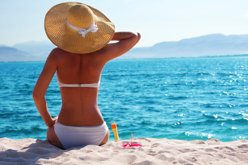 woman in white bikini resting on the beach in straw hat