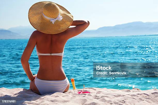 A Woman With A Sun Hat Is Sitting On The Beach Stock Photo - Download Image Now - Women, Sunbathing, Beach