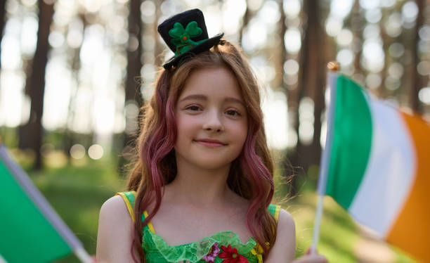 menina ruiva fofa comemorando o dia de são patrício acenando com bandeiras da irlanda - republic of ireland flag human face irish culture - fotografias e filmes do acervo